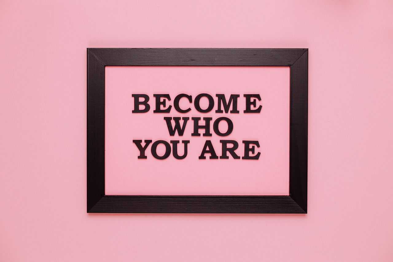 Inspiring quote Become Who You Are framed on a vibrant pink wall, perfect for encouragement.