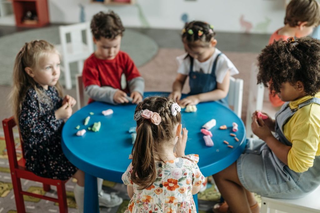 Services Group of preschool children playing with clay at a colorful table in a classroom.
